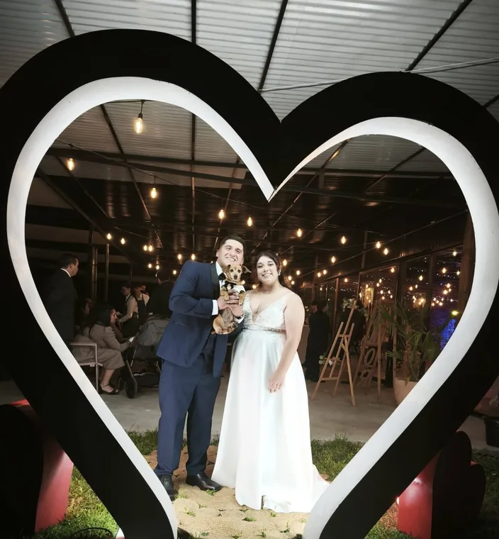 Novios posando bajo un marco de corazón iluminado en su celebración